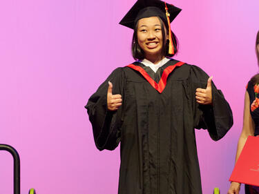 WJ Mouat Grad gives thumbs up in cap and gown