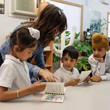 Female Teacher and three male elementary students look at their new books