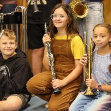 Three students sitting on the floor, holding the new instruments they recieved.